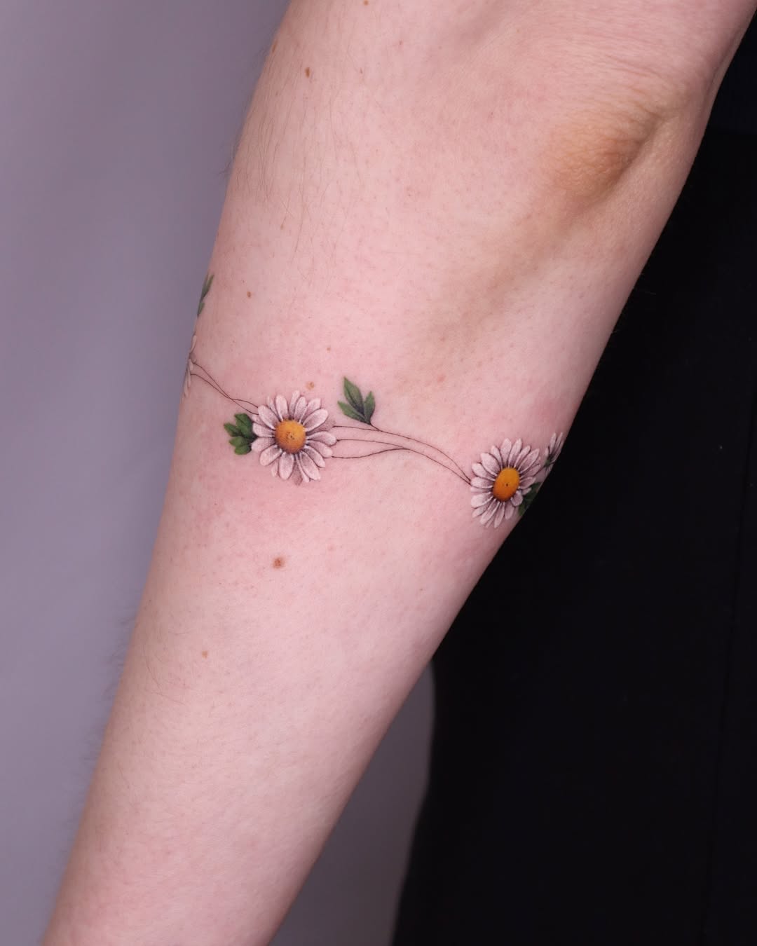 Delicate daisy bracelet tattoo on forearm