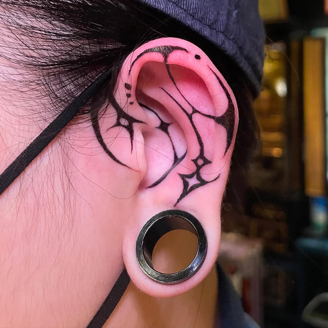 Intricate black outline ear tattoo with stars