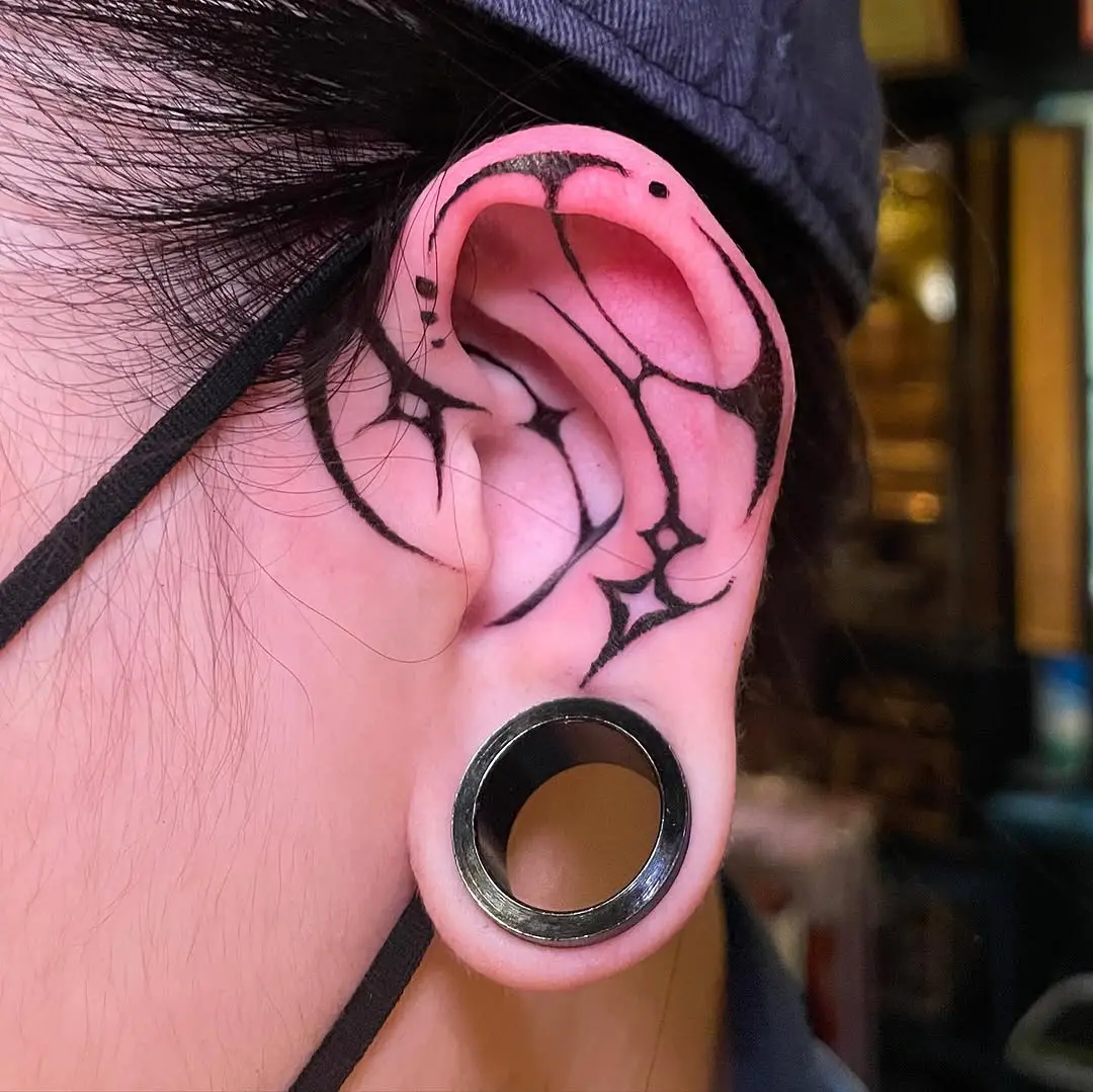 Intricate black outline ear tattoo with stars