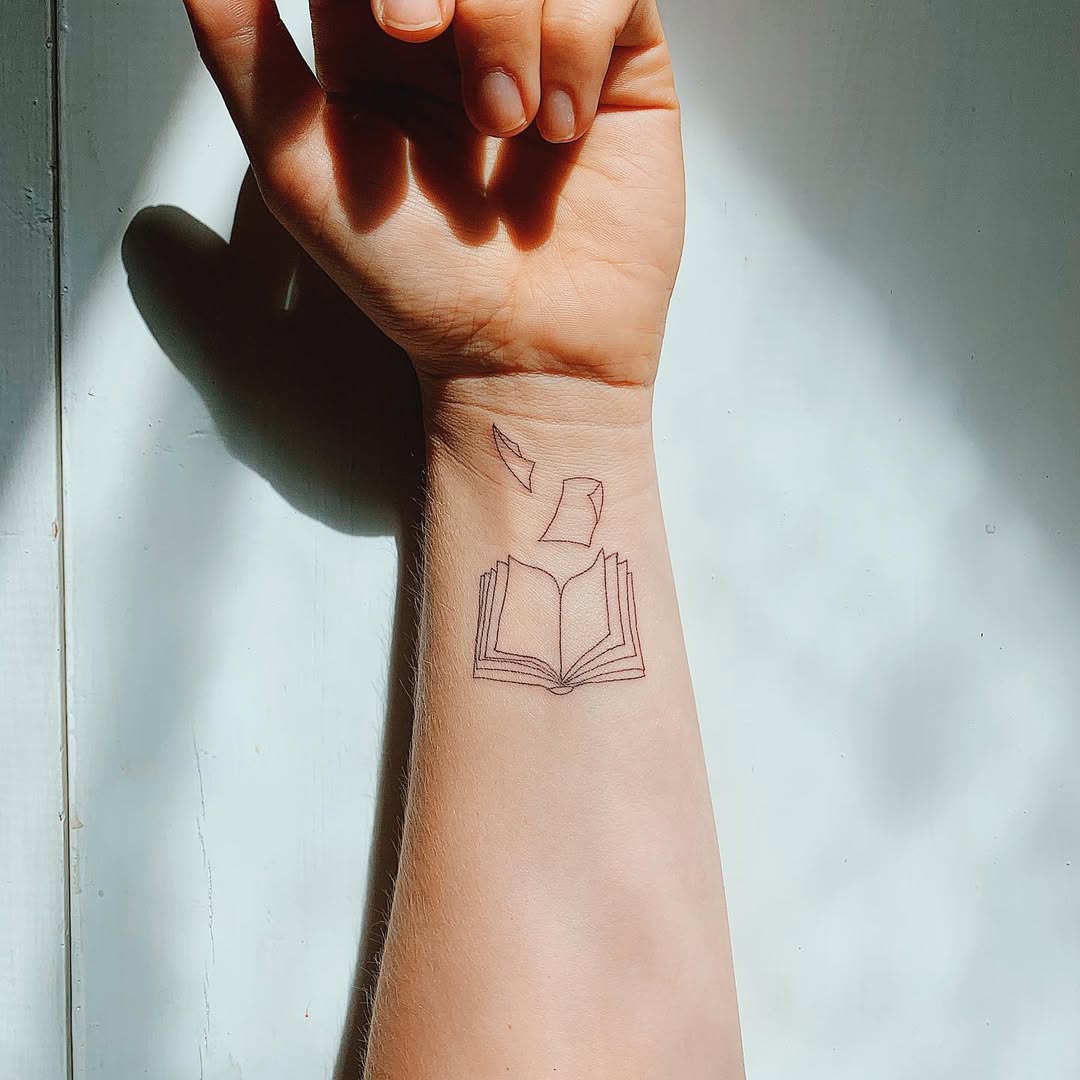 Minimalistic book tattoo with floating pages