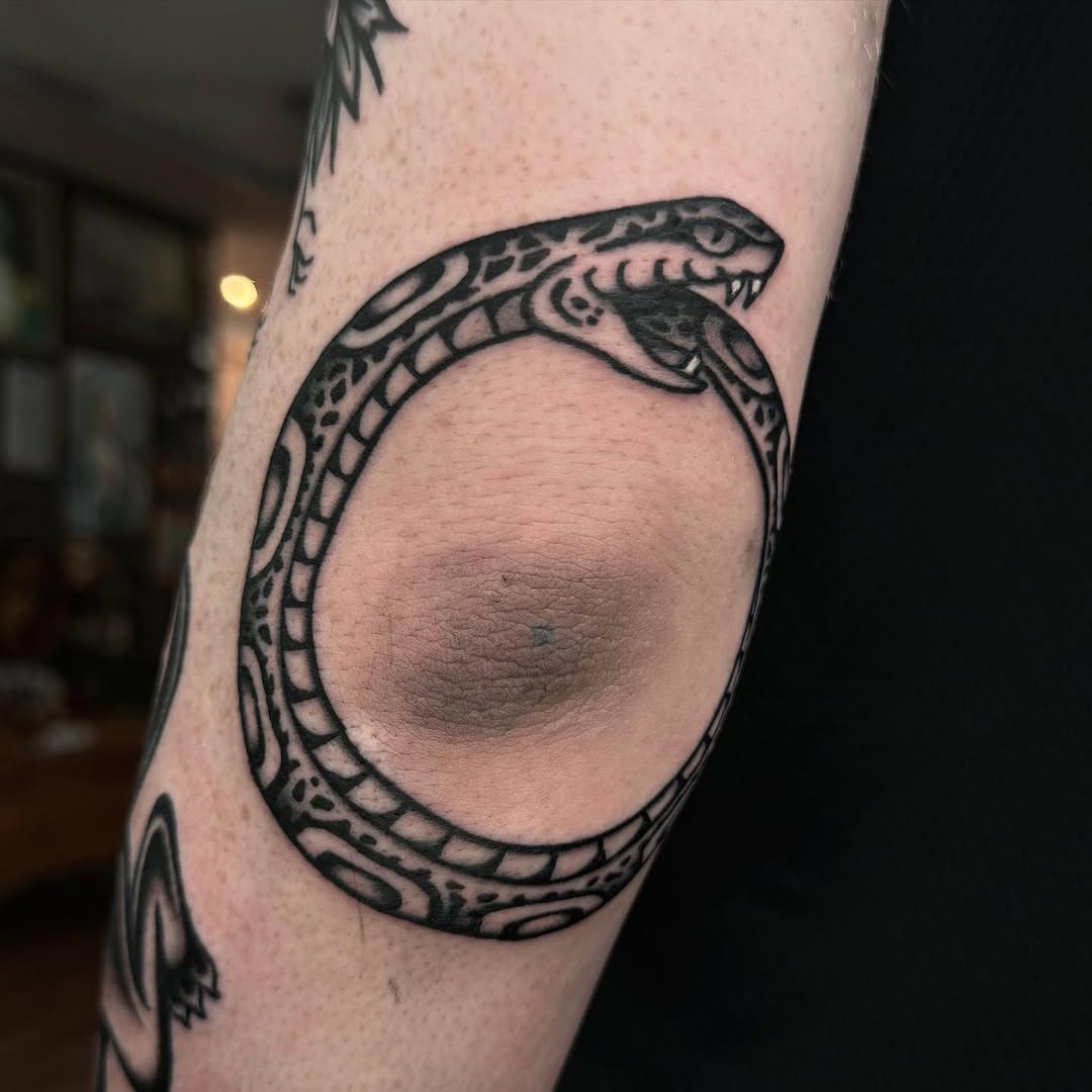 Bold ouroboros tattoo wrapping around elbow.