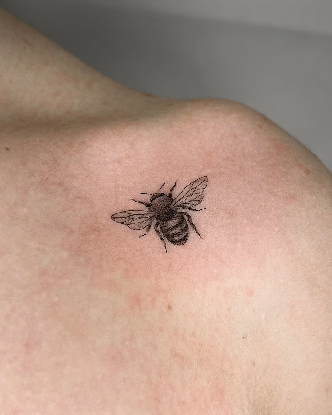 Elegant minimalistic bee tattoo design on shoulder