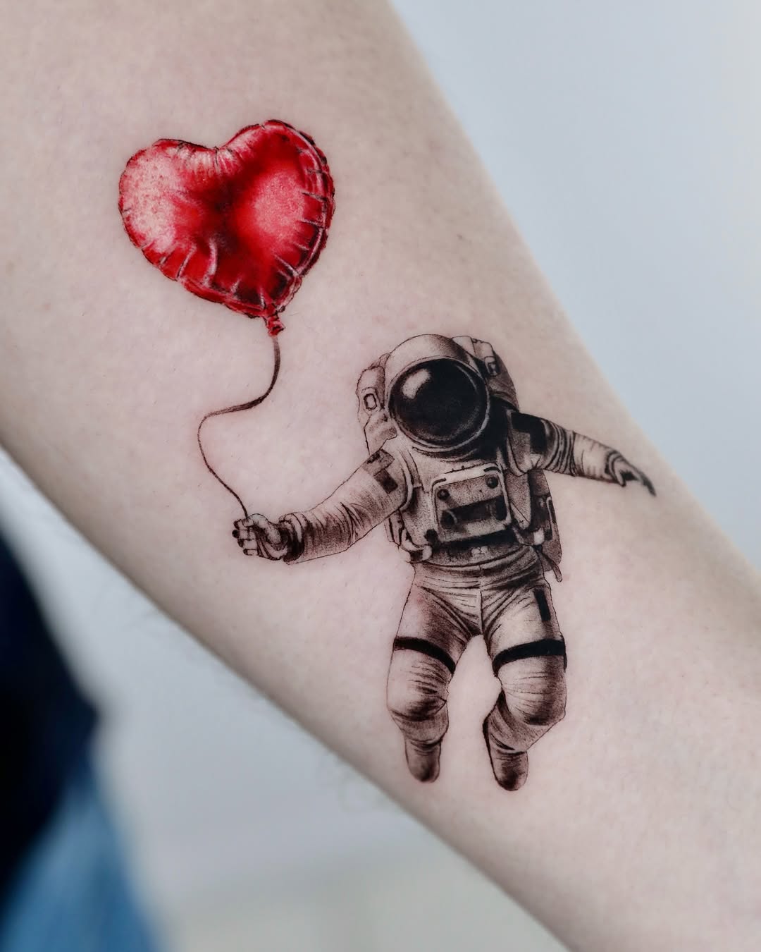 Whimsical astronaut holding a heart balloon tattoo