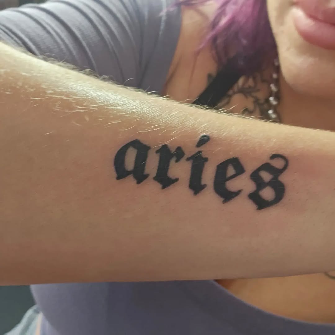 Bold Script Aries Tattoo on Forearm