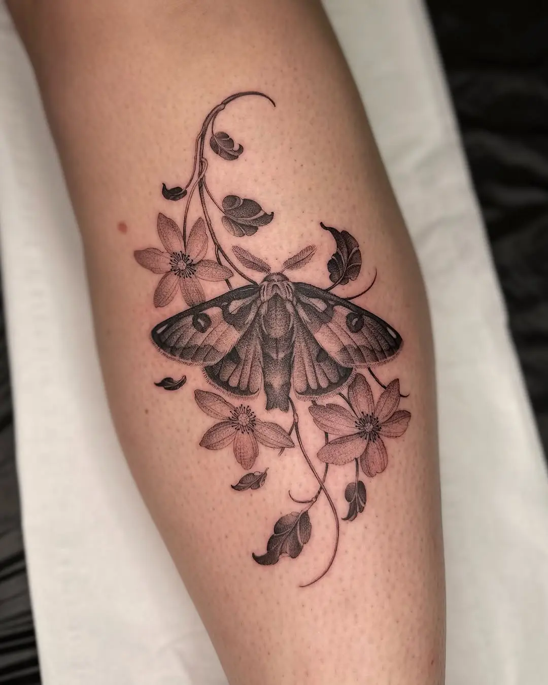 Intricate moth tattoo surrounded by floral elements