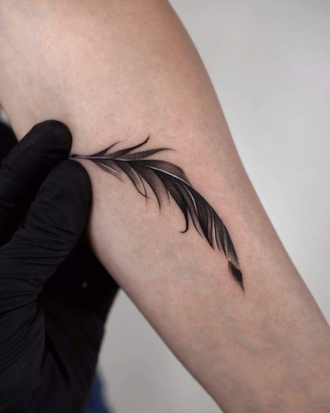 Elegant black feather tattoo design on arm