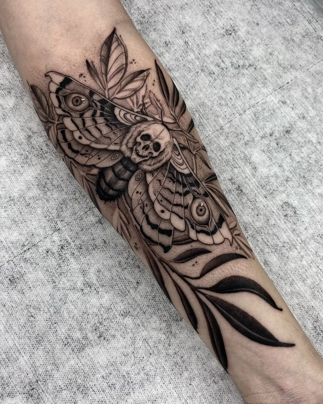 Intricate forearm moth tattoo with leaves and skull