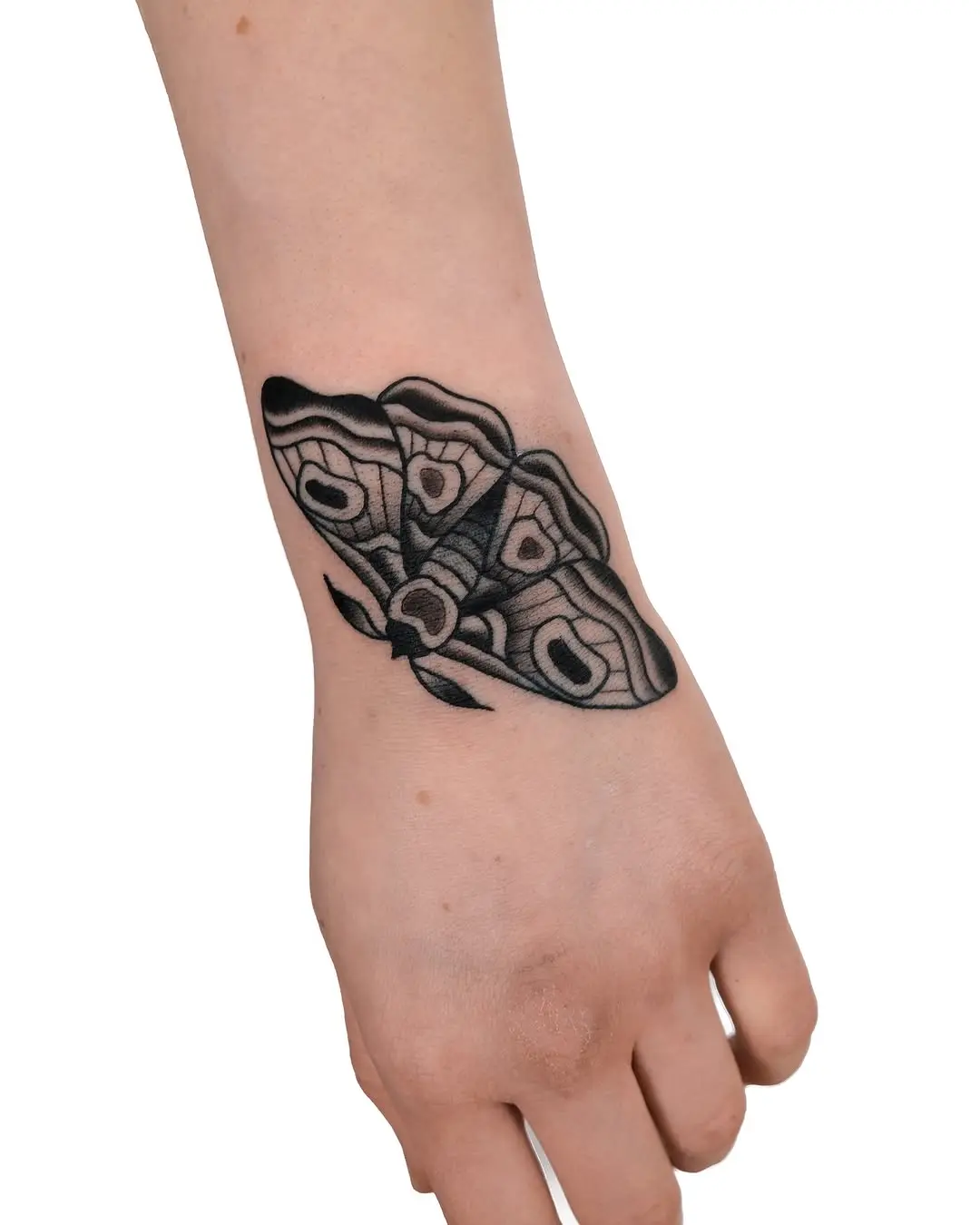 Intricate black line moth tattoo on forearm