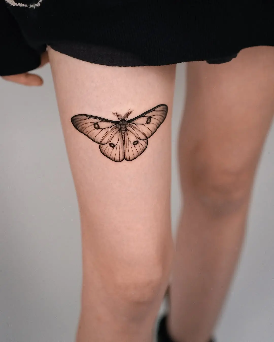 Elegant black line moth tattoo on thigh