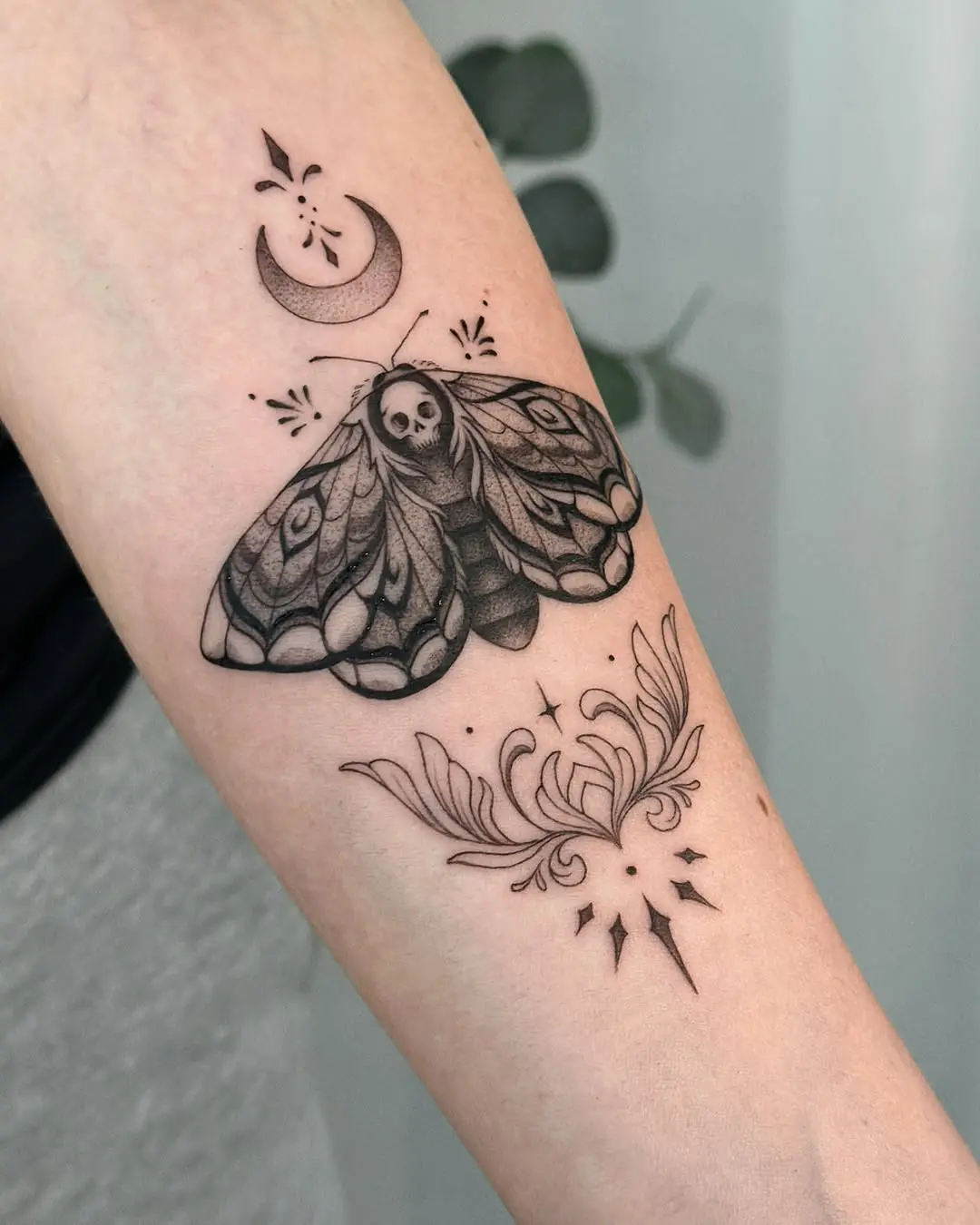 Intricate moth tattoo with moon and floral elements.
