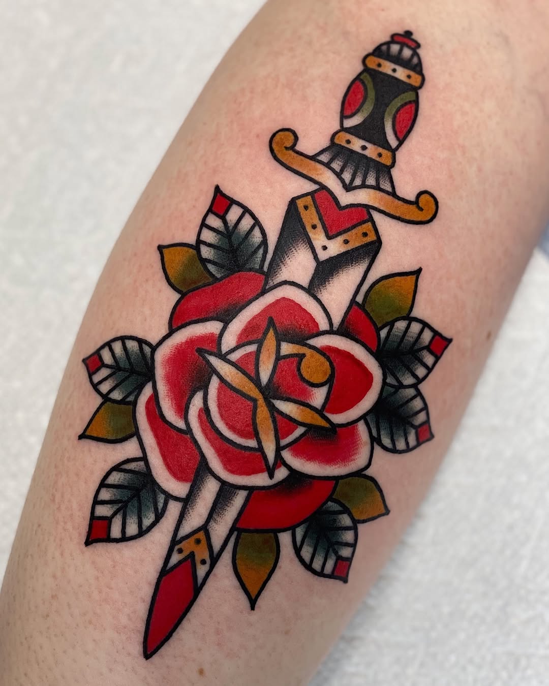 Bold rose tattoo with dagger and leaves