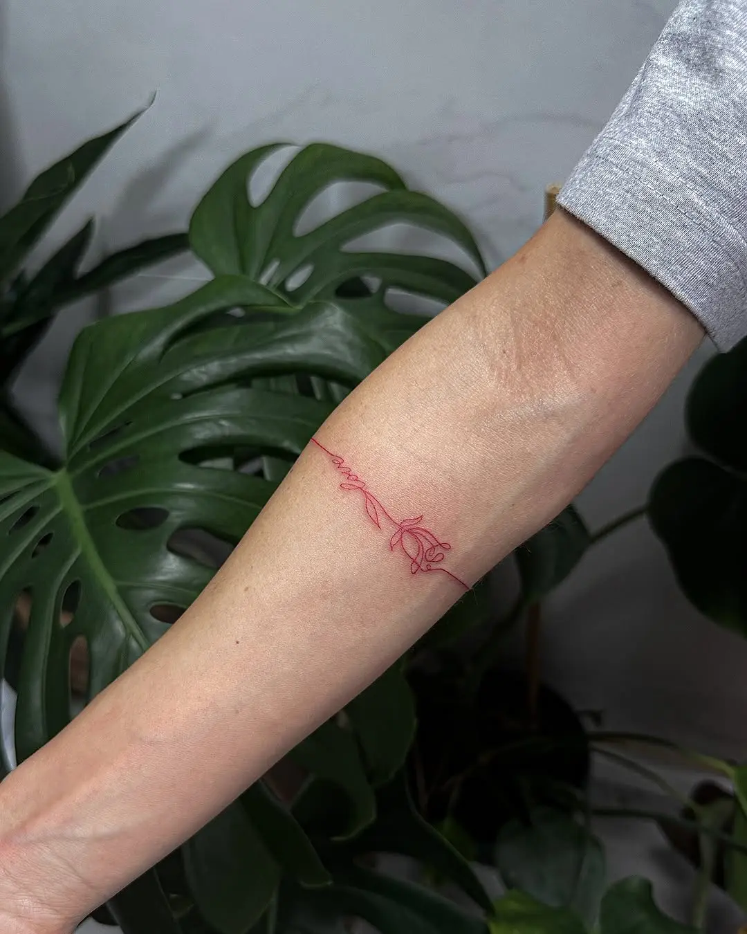 Delicate red floral line tattoo on the forearm