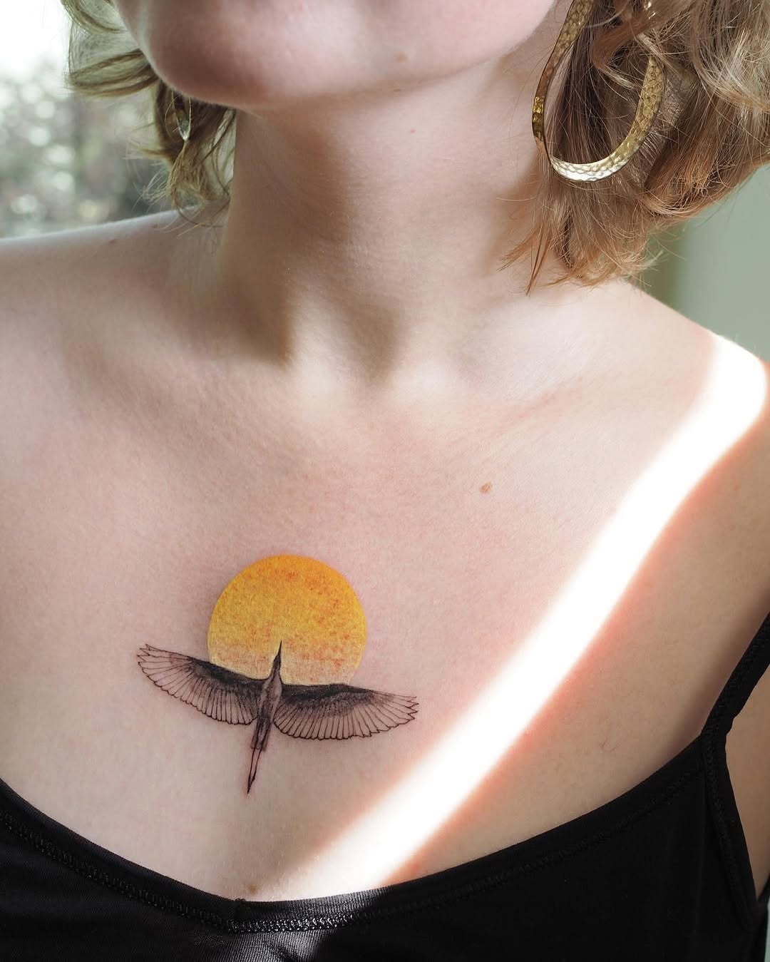 Elegant bird tattoo against a vibrant sun