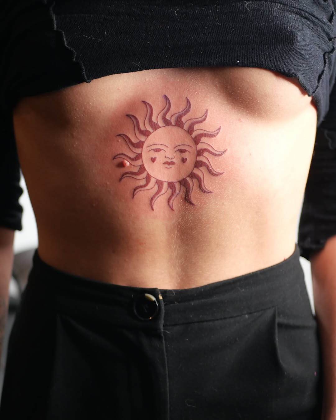 Radiant sun tattoo with playful facial features