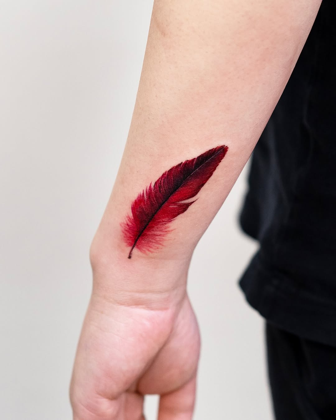 Bold red feather tattoo on forearm