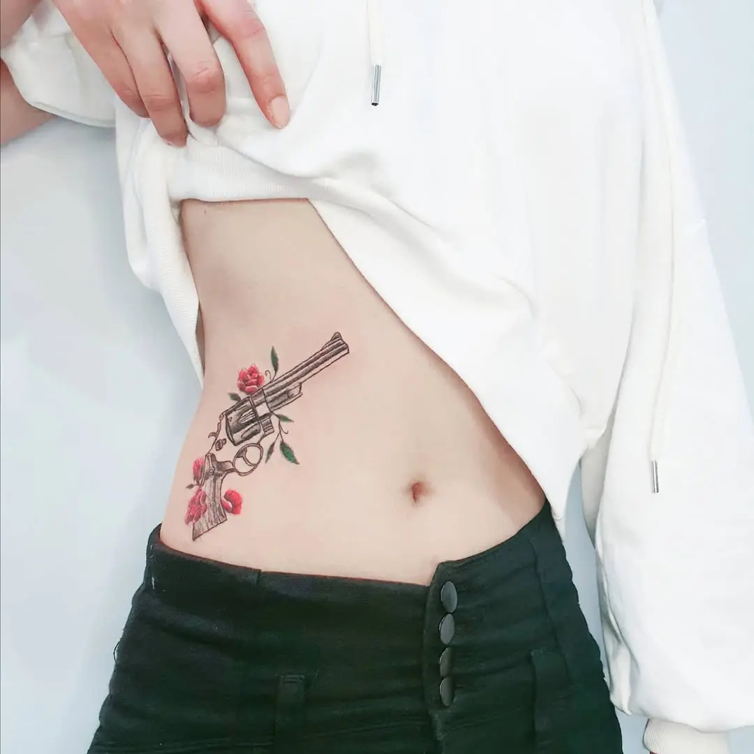 Bold waist tattoo combining gun and flowers
