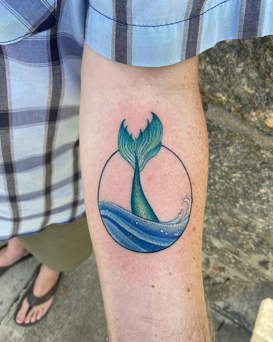 Whimsical whale tail tattoo with water waves