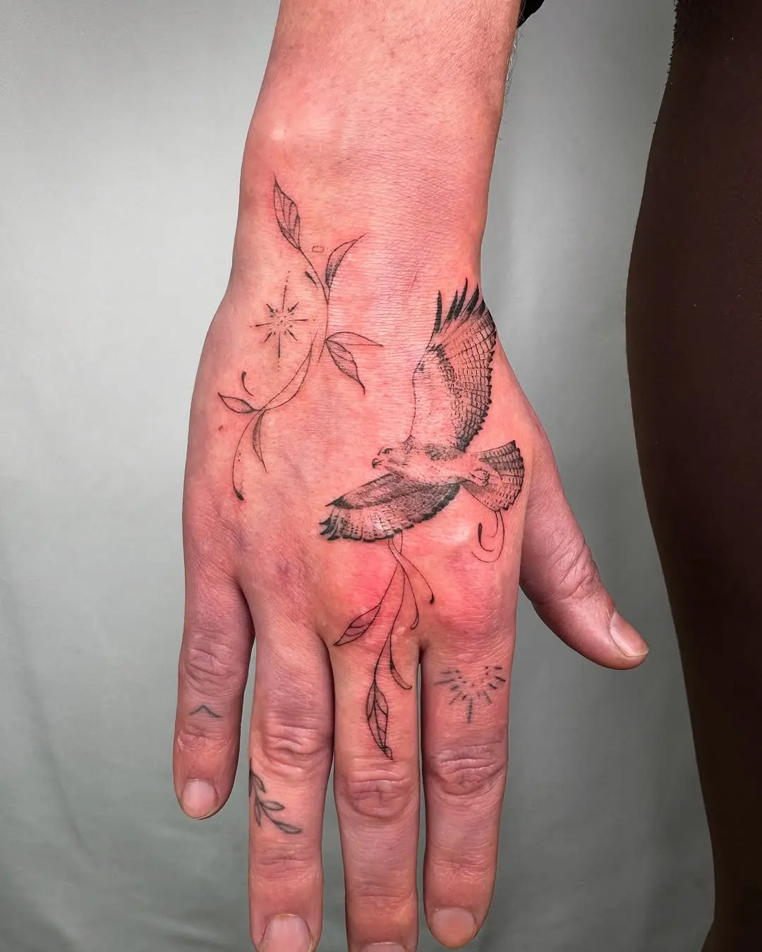 Elegant hawk tattoo with floral elements on hand