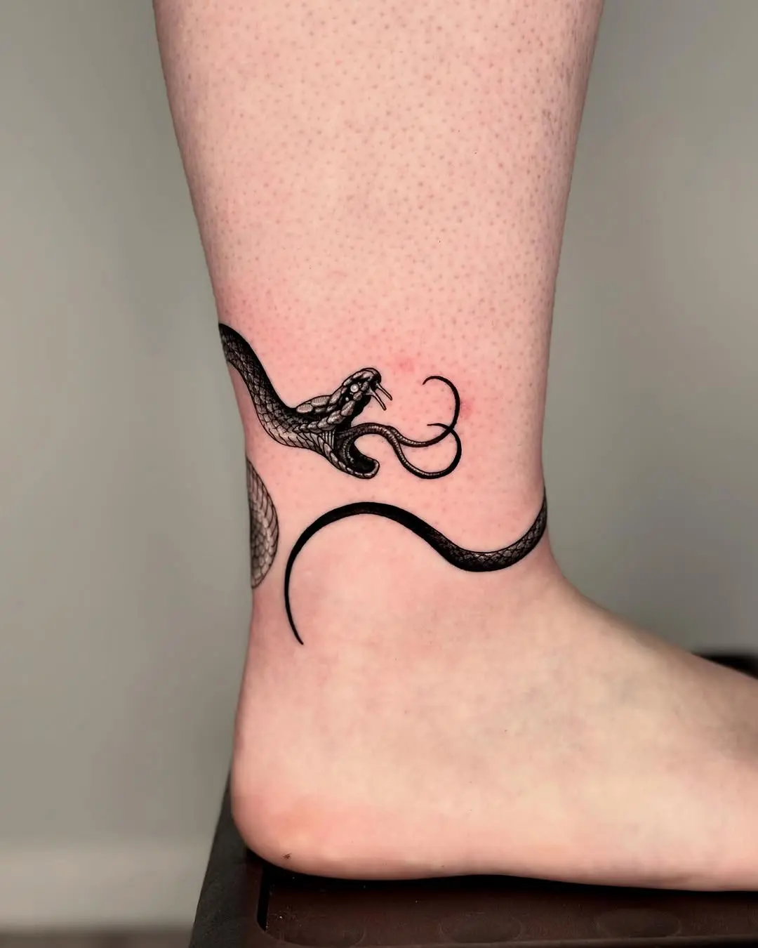 Elegant black snake tattoo on ankle area