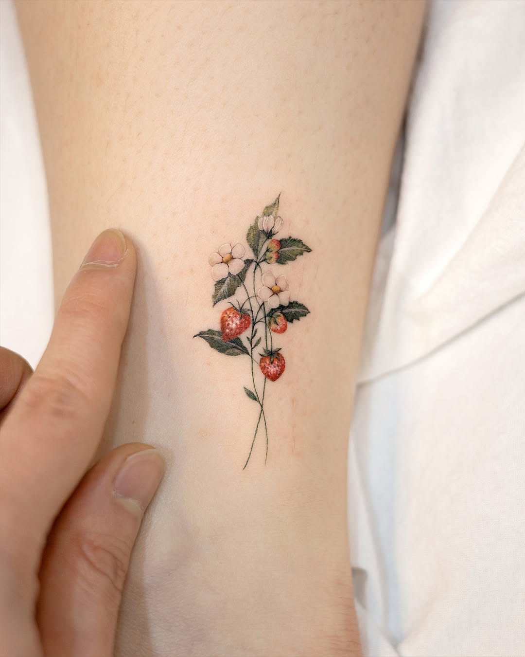 Delicate strawberry and flower tattoo on skin