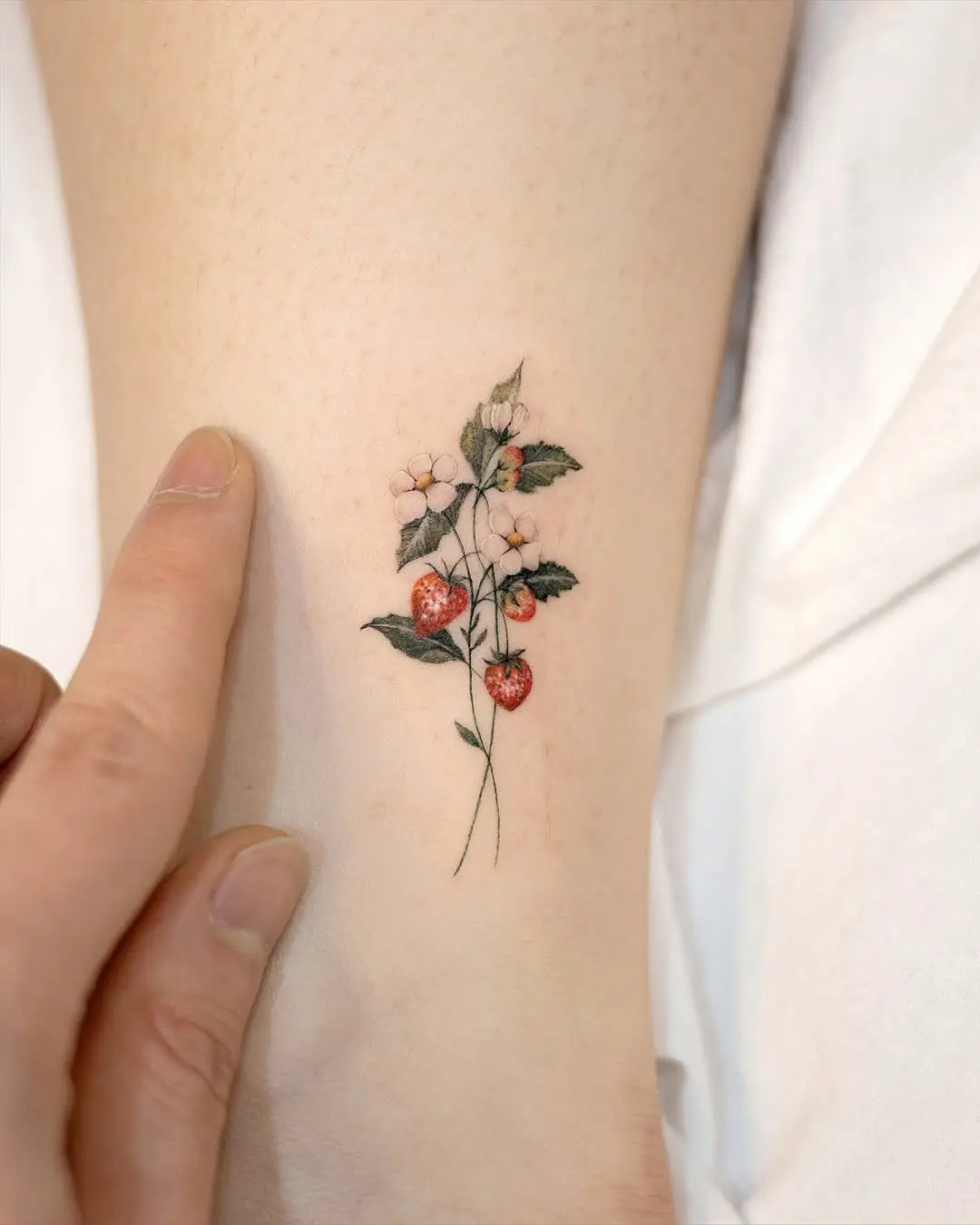 Delicate strawberry and flower tattoo on skin