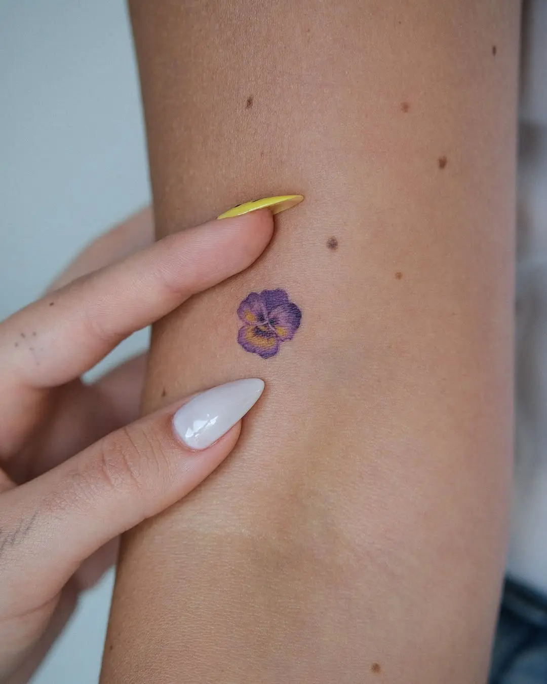 Delicate purple pansy flower tattoo on arm