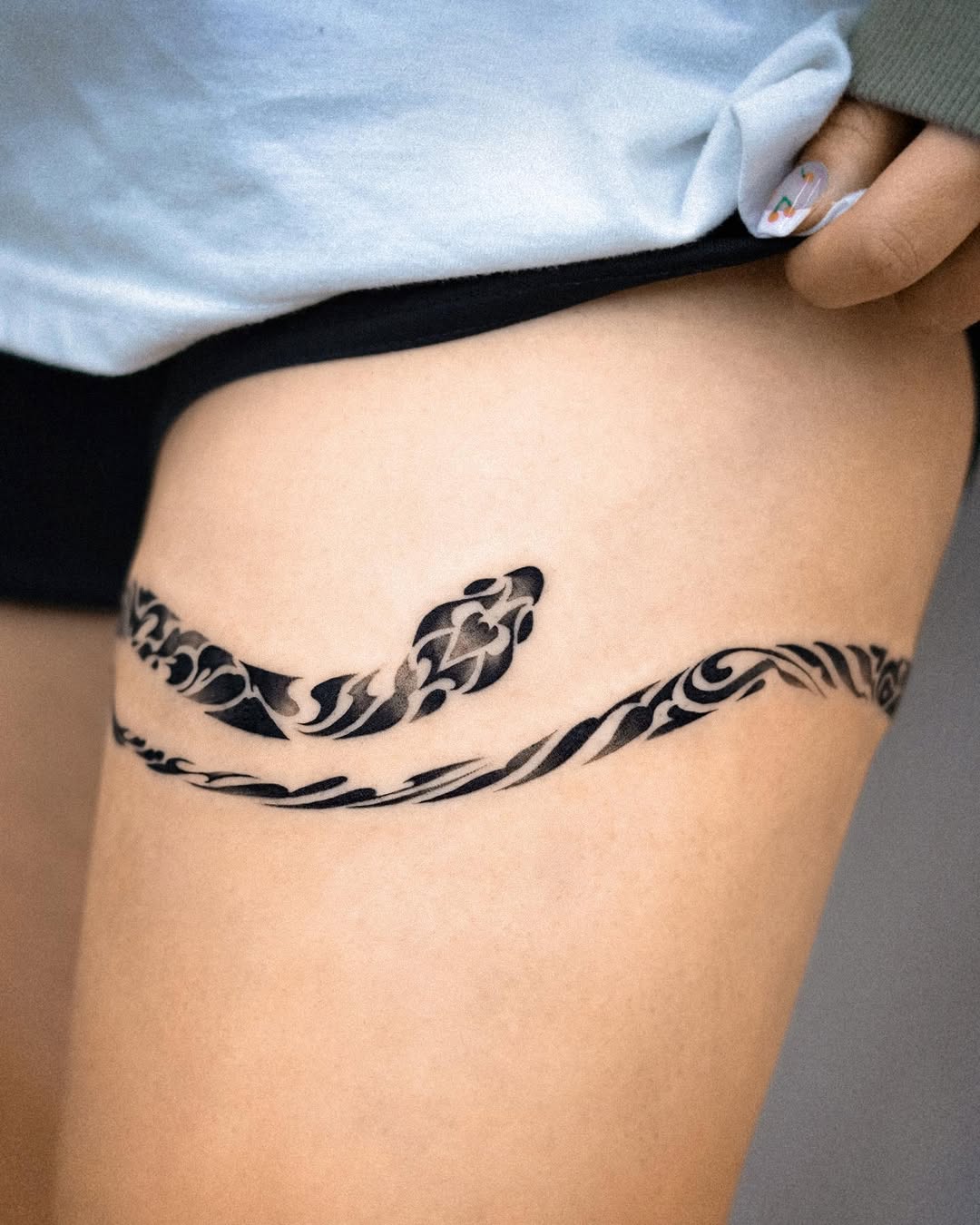 Minimalist snake tattoo flowing elegantly on thigh.