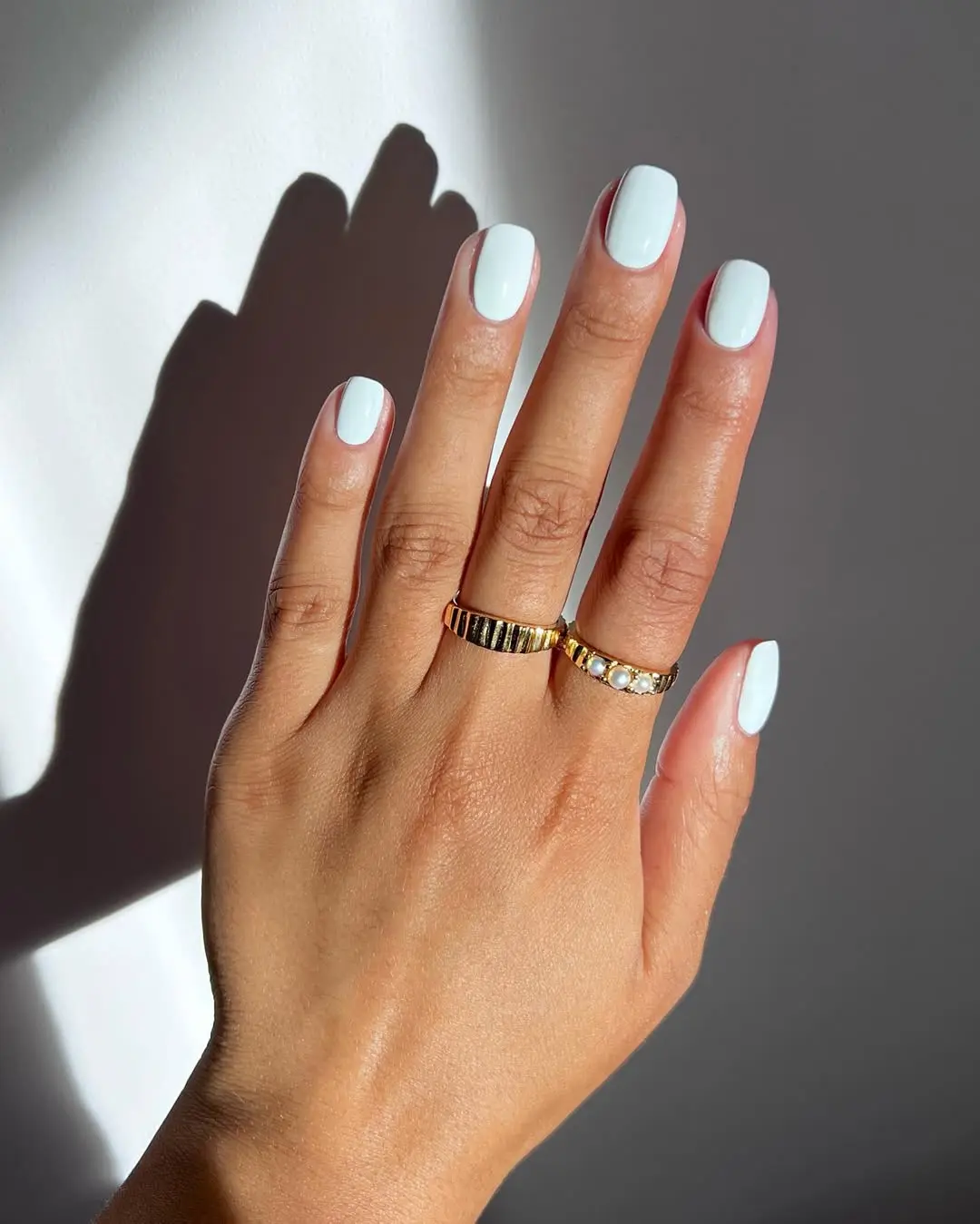 Elegant white nails adorned with gold rings
