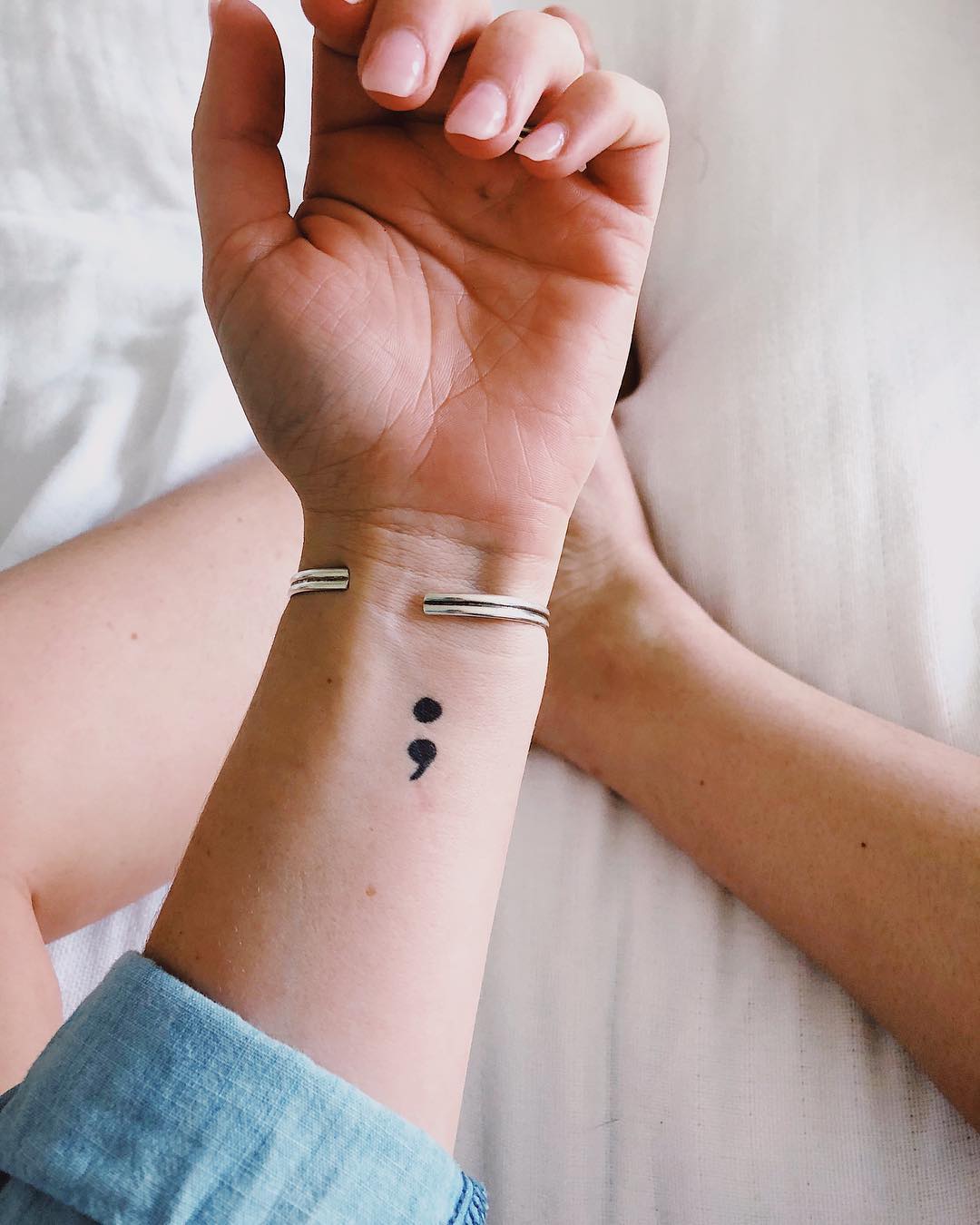Minimalist semicolon tattoo on a wrist.
