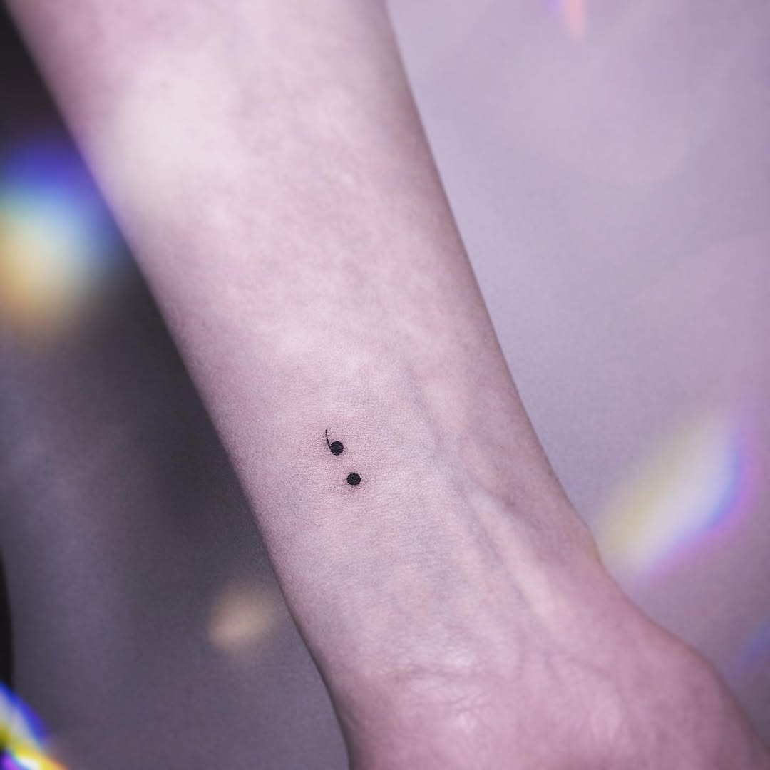 Minimalist semicolon tattoo on forearm