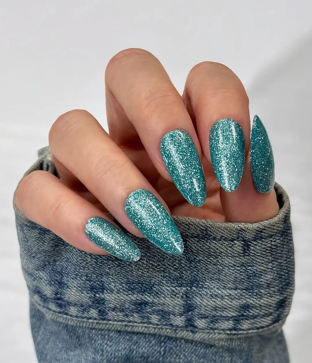 Sparkling teal nails against denim backdrop