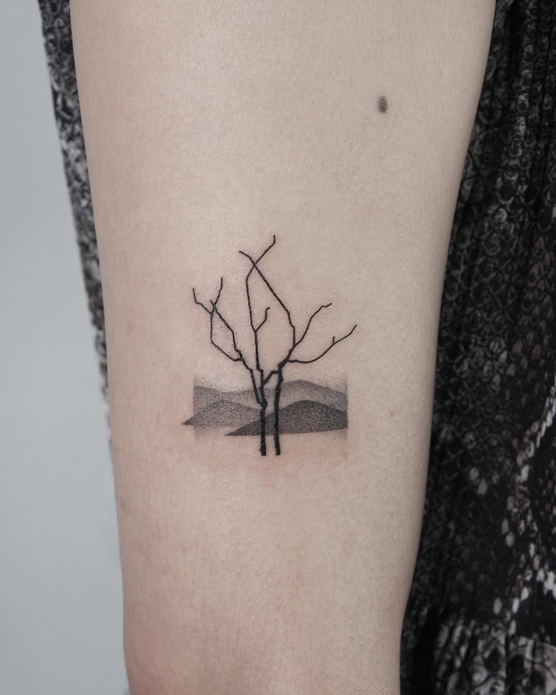 Minimalist tree tattoo with a serene landscape