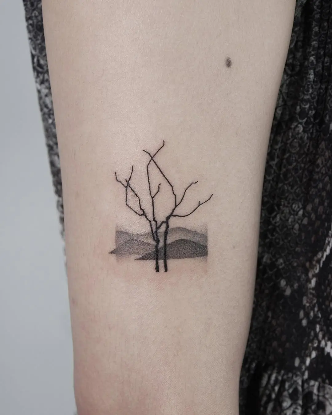 Minimalist tree tattoo with a serene landscape