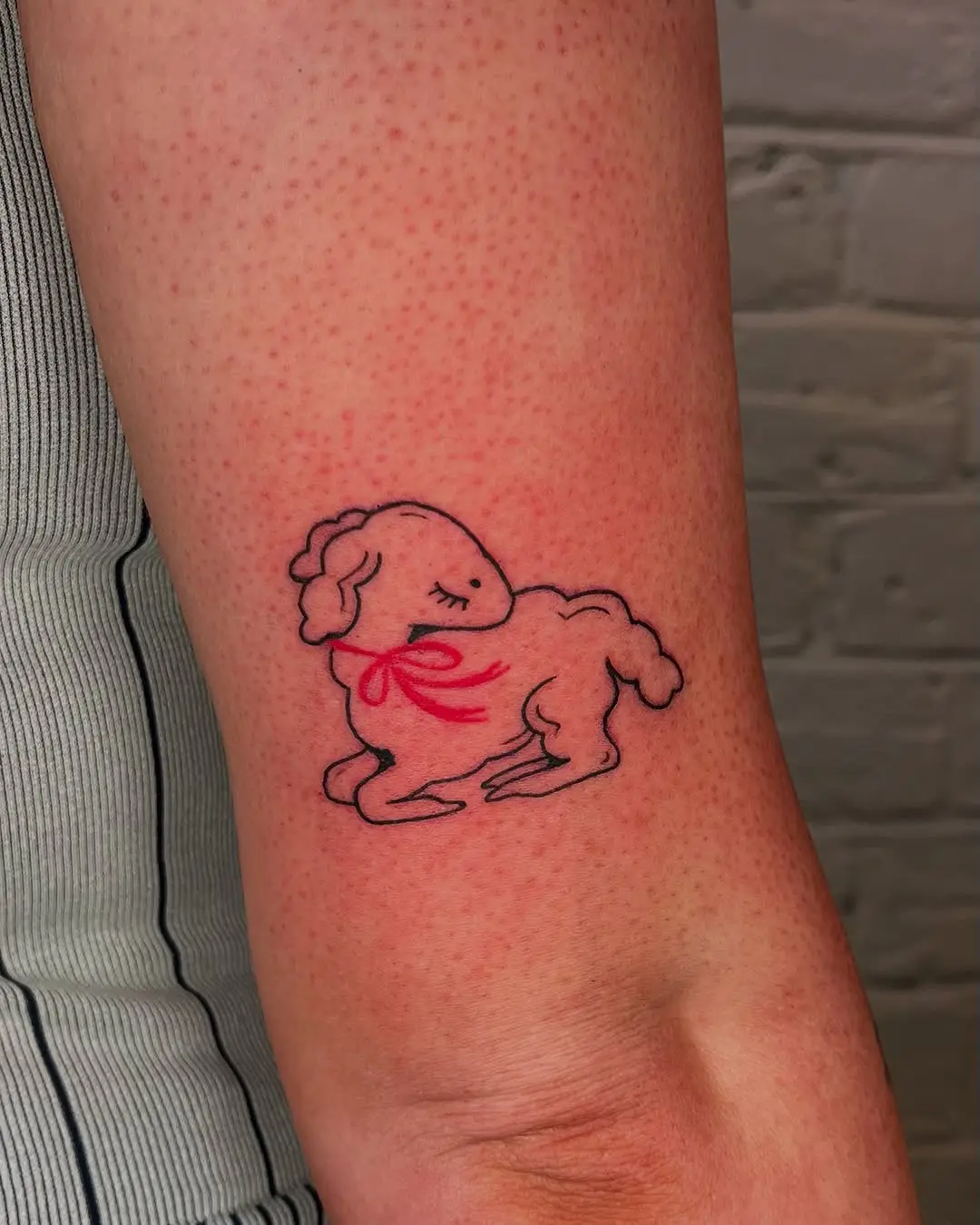 Playful lamb tattoo with a charming red ribbon