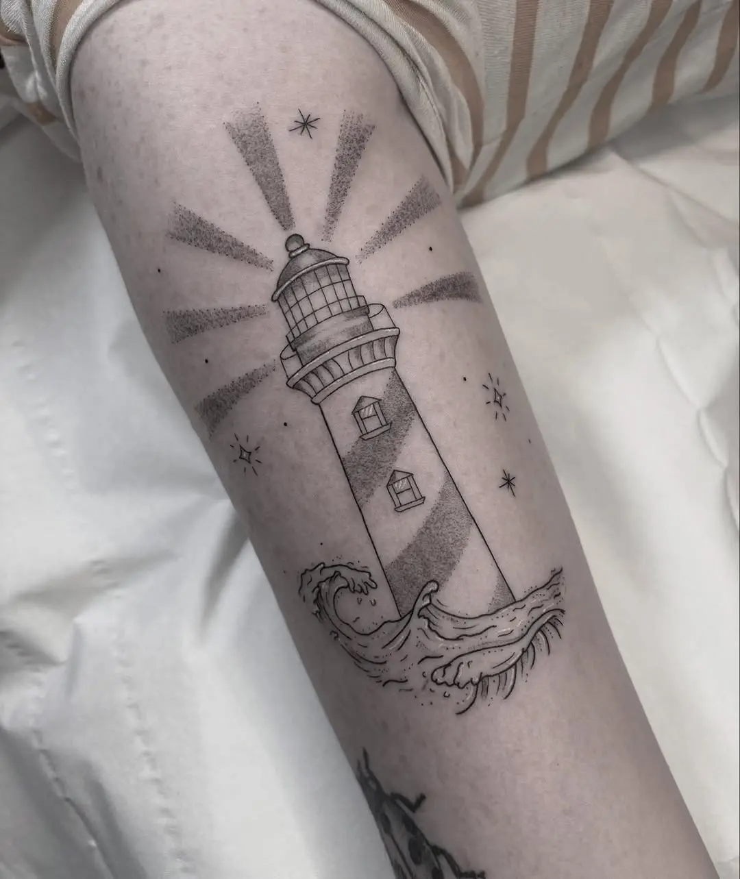 Intricate lighthouse tattoo with radiant waves