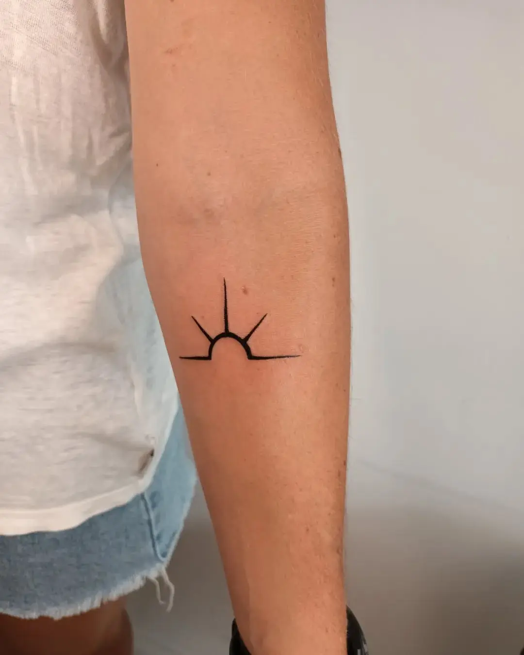 Minimalist black sunrise tattoo on arm