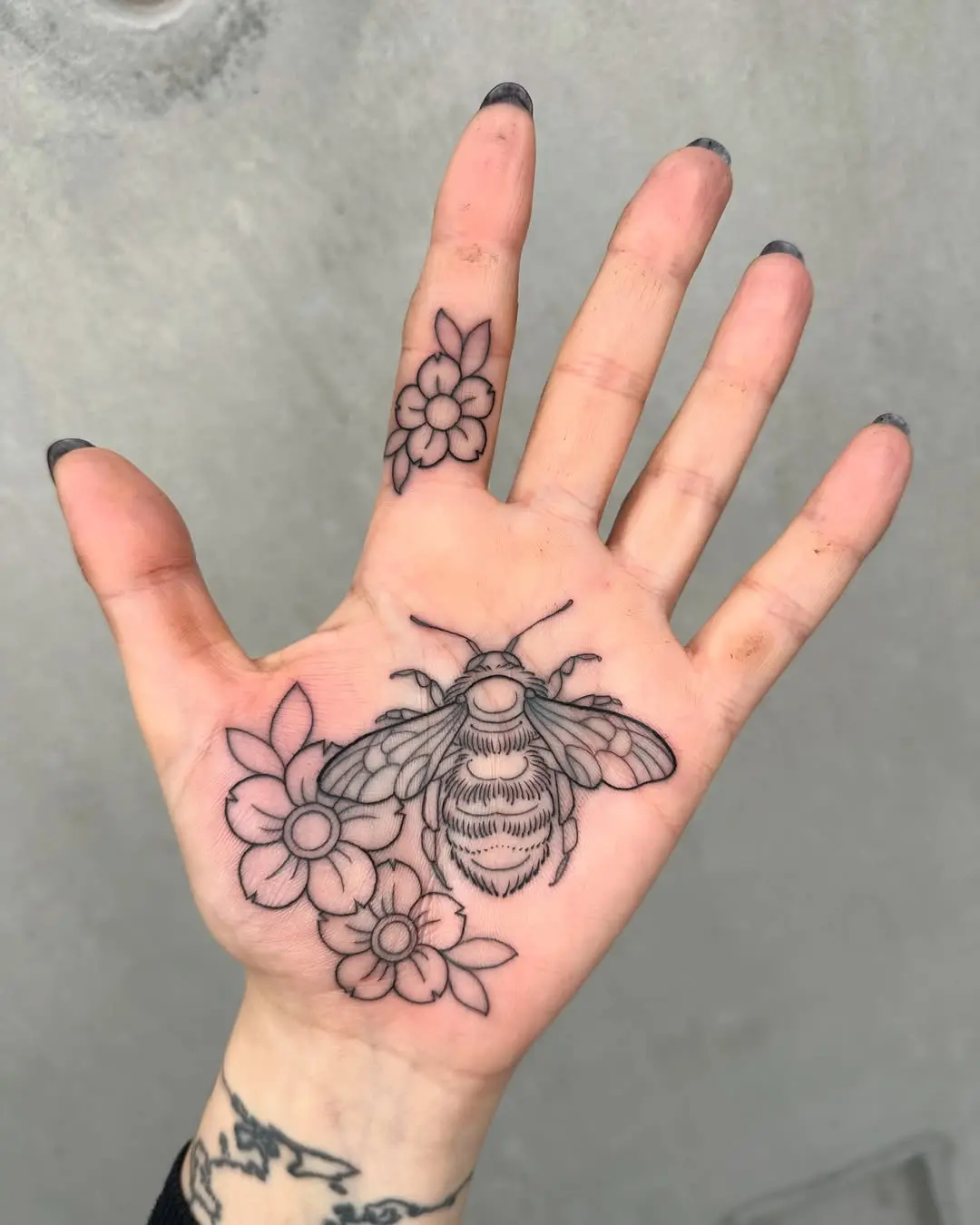 Intricate palm tattoo featuring bee and flowers