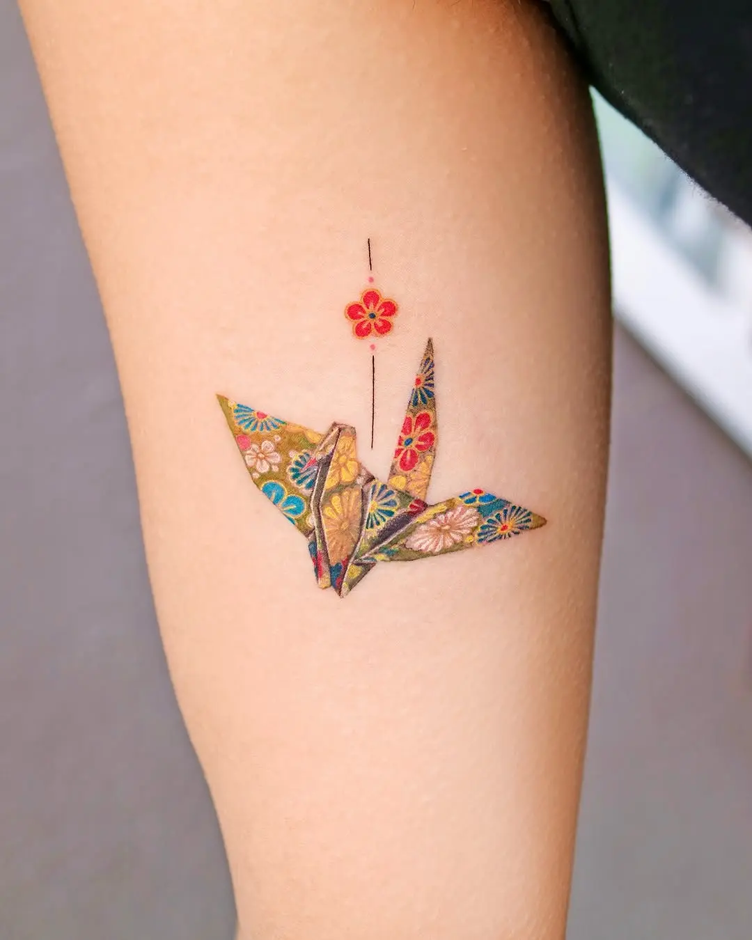 Vibrant origami crane tattoo with floral details