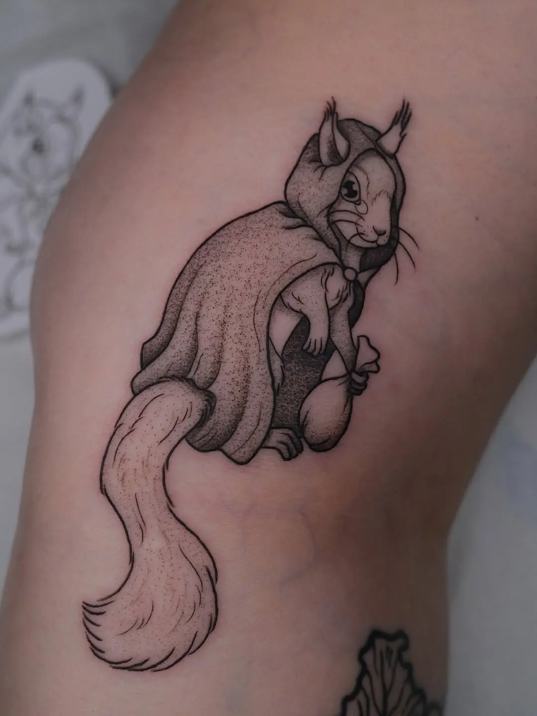 Whimsical squirrel tattoo in a cozy hooded cloak