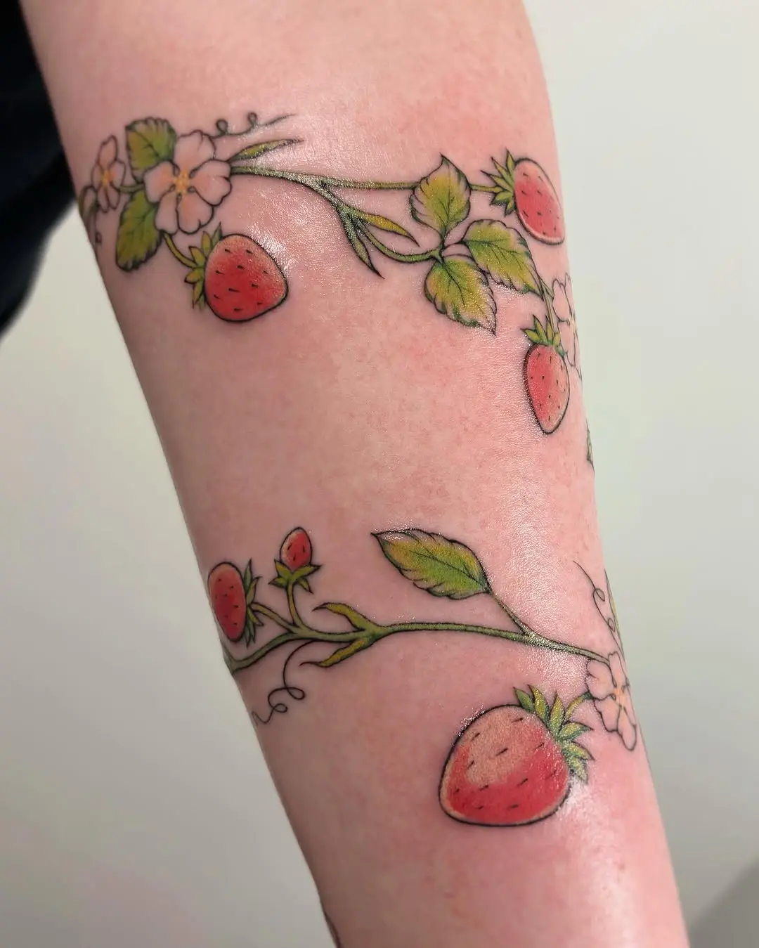 Whimsical strawberry tattoo with floral accents