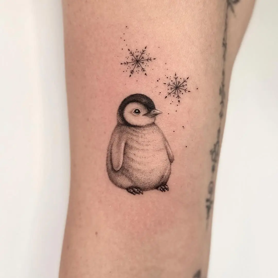 Charming penguin tattoo surrounded by snowflakes.