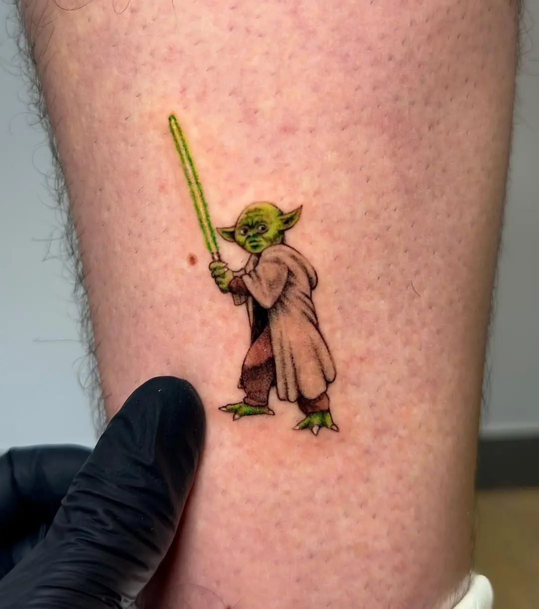 Playful Yoda with lightsaber tattoo on skin