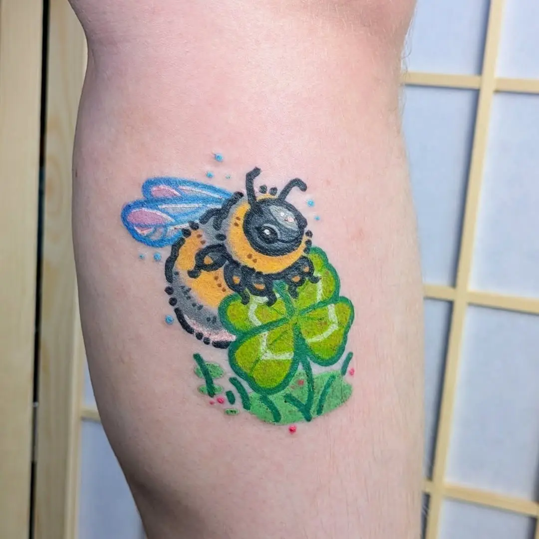 Colorful bee atop a four-leaf clover tattoo.