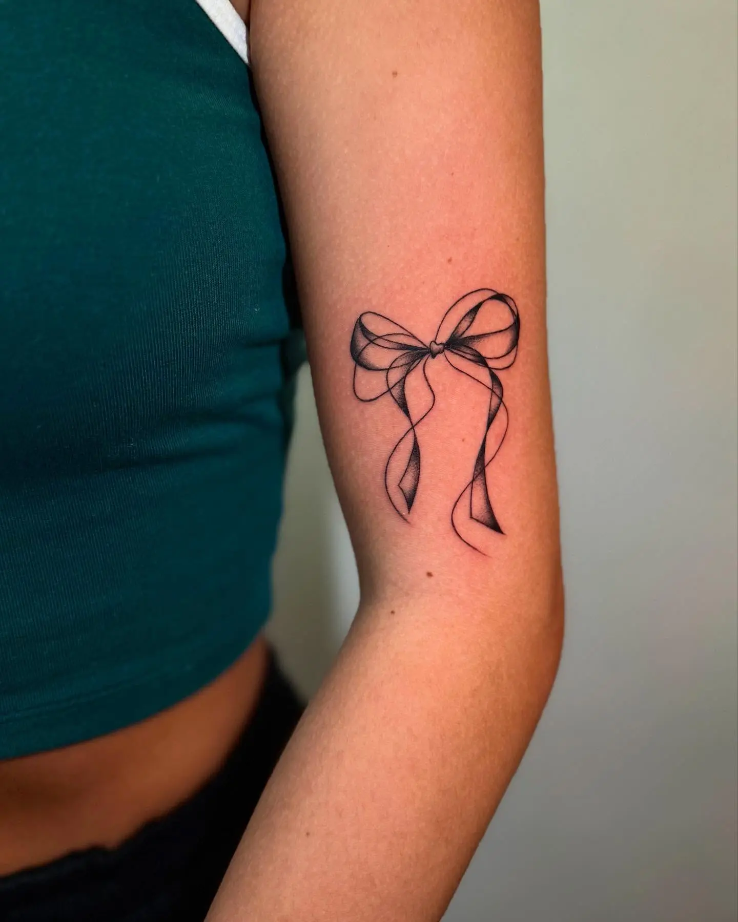 Elegant black line bow tattoo on arm