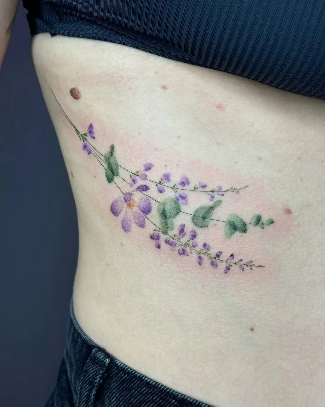 Delicate eucalyptus and floral rib tattoo design