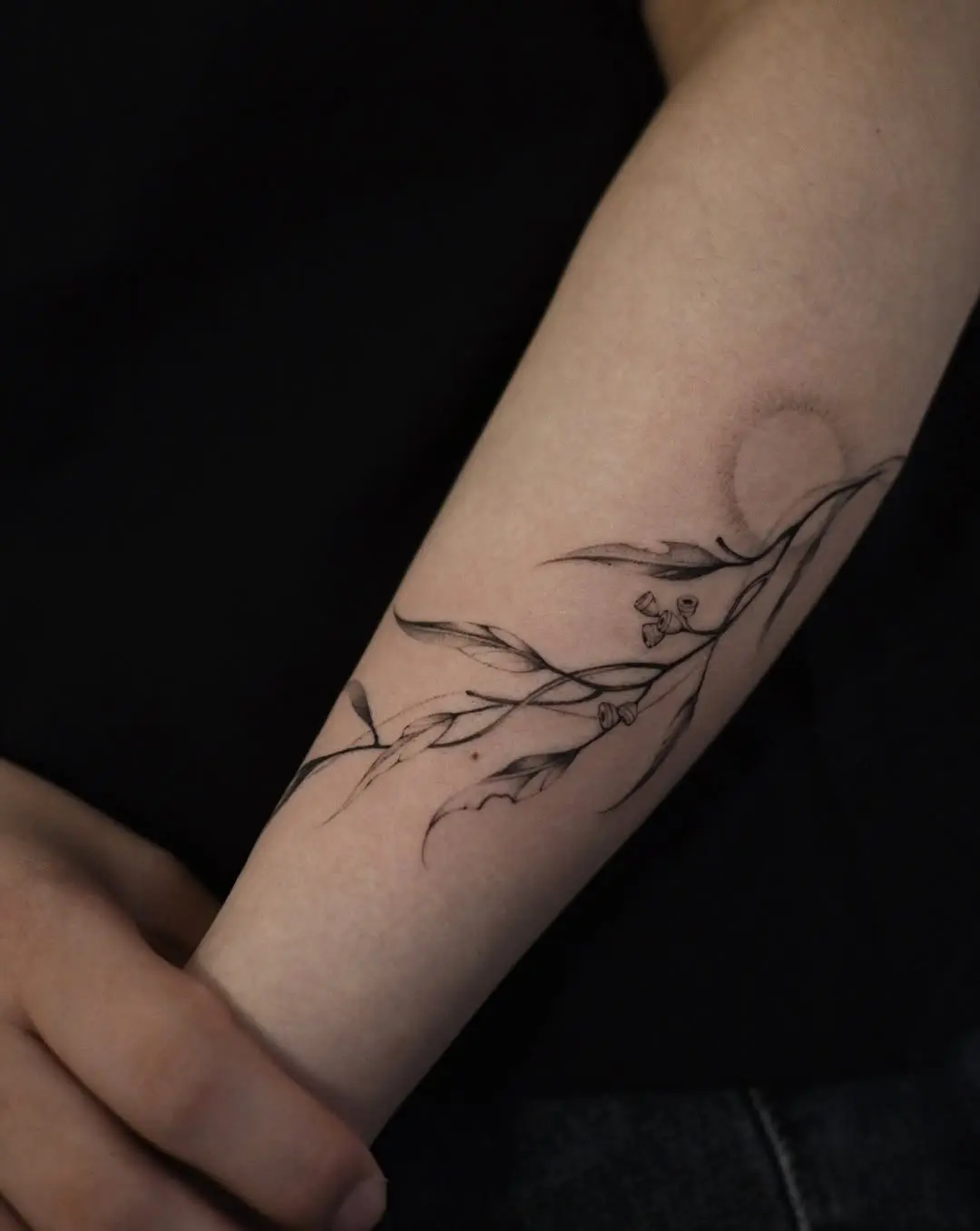 Elegant eucalyptus branch tattoo with a subtle sun