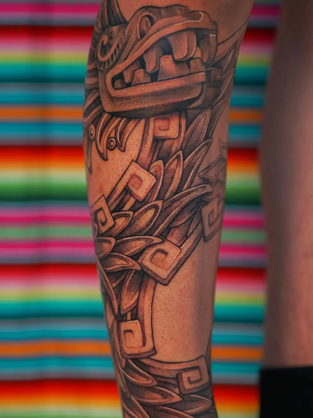 Intricate Aztec leg tattoo with vibrant backdrop