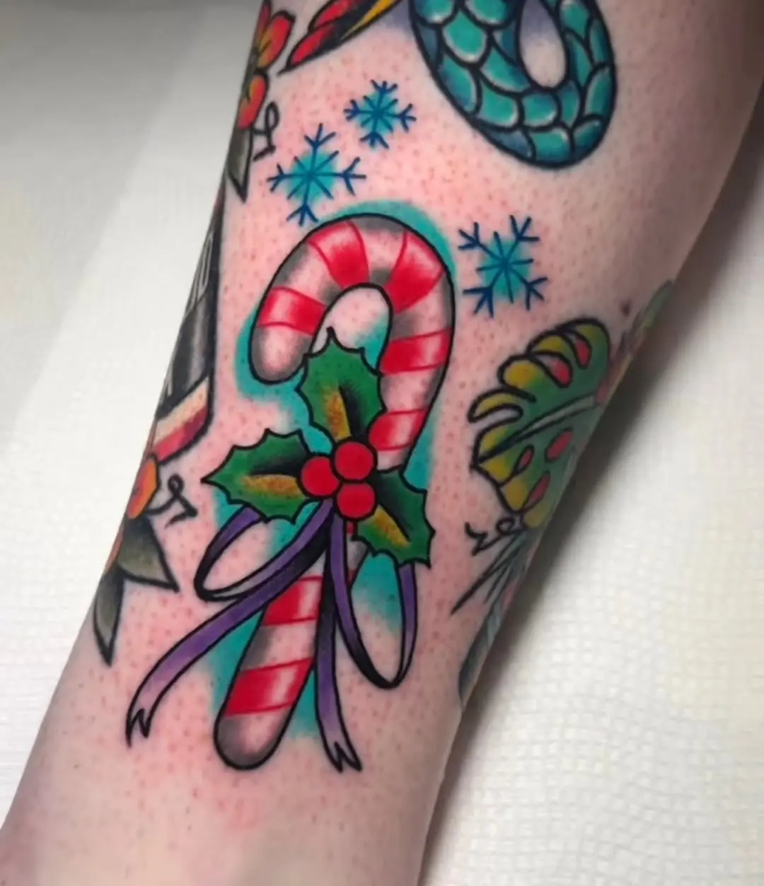 Vibrant candy cane tattoo with holly details