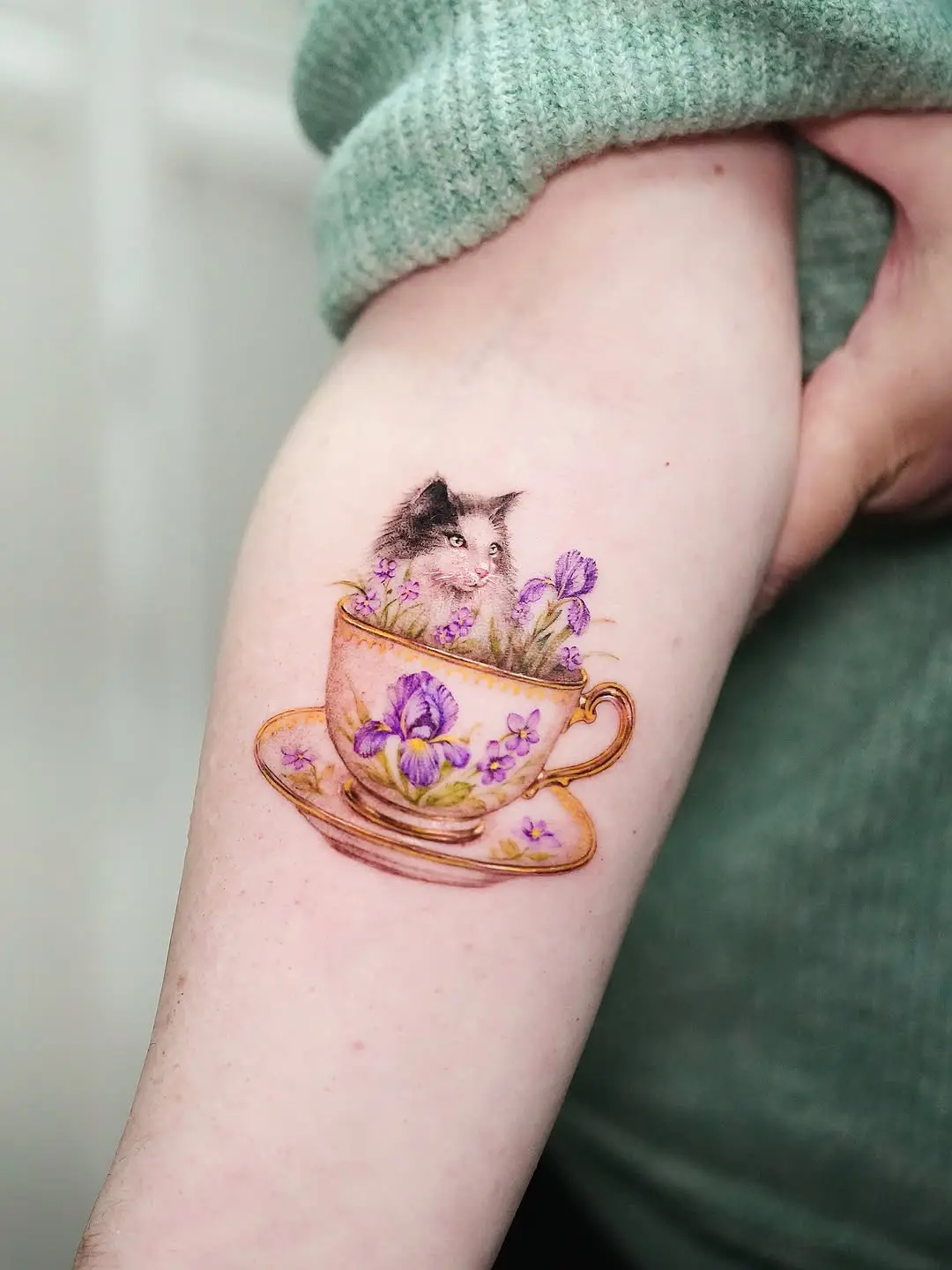Charming violet-themed cat in a teacup tattoo