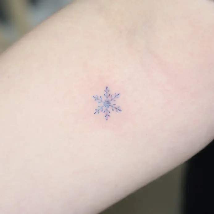Delicate blue snowflake tattoo on the arm